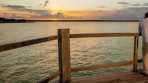 A wooden pier with a railing overlooking a body of water during sunset. - Queen-size bed, with a private bathroom, a walk-in shower and closet. (Orchid Bay)