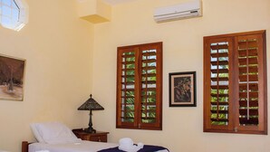 A hotel room with two beds, a nightstand, a lamp, and two windows with wooden shutters.