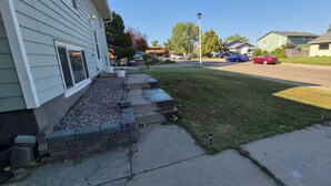 Une rue résidentielle bordée de maisons, avec un trottoir et des voitures garées.