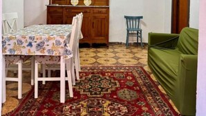 A dining area with a wooden cabinet, a table with chairs, a green sofa, and a patterned rug. - Vacation home Hause le Gallinelle. (Assemini)
