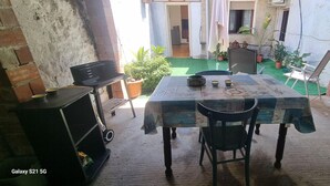 A small, rustic dining area with a table set for two, a grill, and potted plants. - Vacation home Hause le Gallinelle. (Assemini)