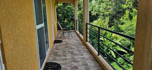 A balcony with a tiled floor, a chair, and a railing overlooking a lush green landscape. - Spacious 2-Bedroom Apartment (1080 sqft) Fully Furnished, Quiet & Green Retreat (Morne Jaloux Ridge)