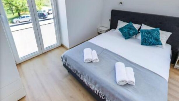 Ett modernt hotellrum med en stor säng, två kuddar och utsikt över en parkeringsplats genom en skjutdörr.