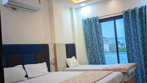 A hotel room with two beds, a large window with curtains, an air conditioning unit, and a view of the outside. - Hotel Moad Mudgal Palace (Khandwa)