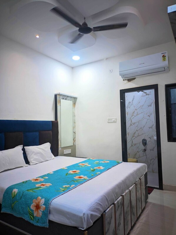 Une chambre à coucher comprenant un lit, un ventilateur de plafond, un appareil de climatisation, un miroir et une porte ornée d’un motif rappelant le marbre.