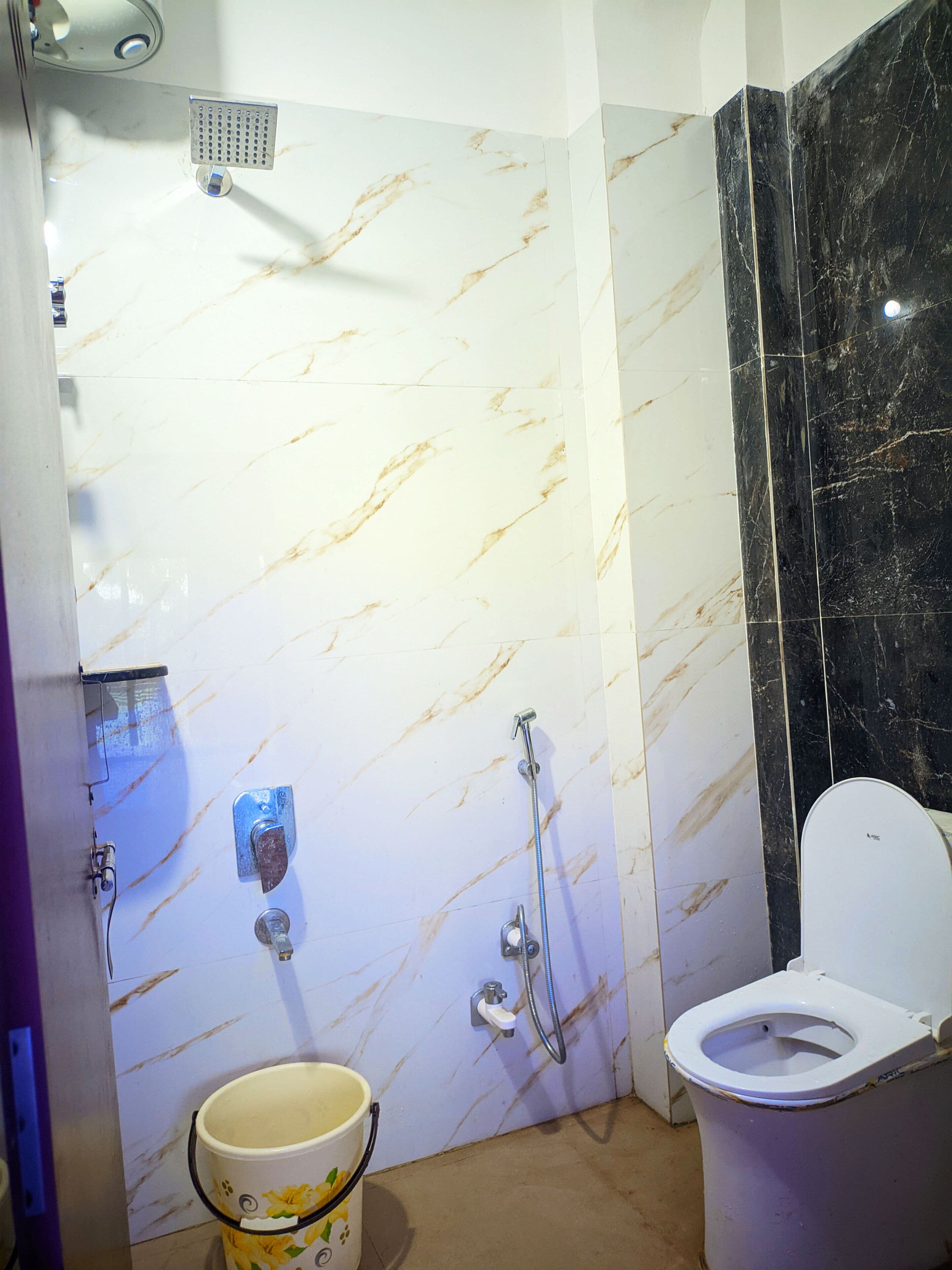 A bathroom with a white marble wall, a black marble accent wall, a white toilet, and a shower with a handheld showerhead.