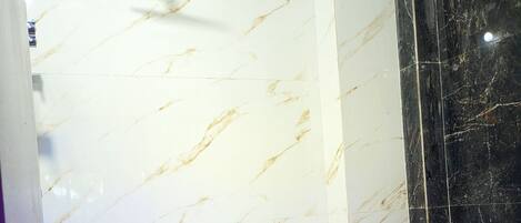 A bathroom with a white marble wall, a black marble accent wall, a white toilet, and a shower with a handheld showerhead.