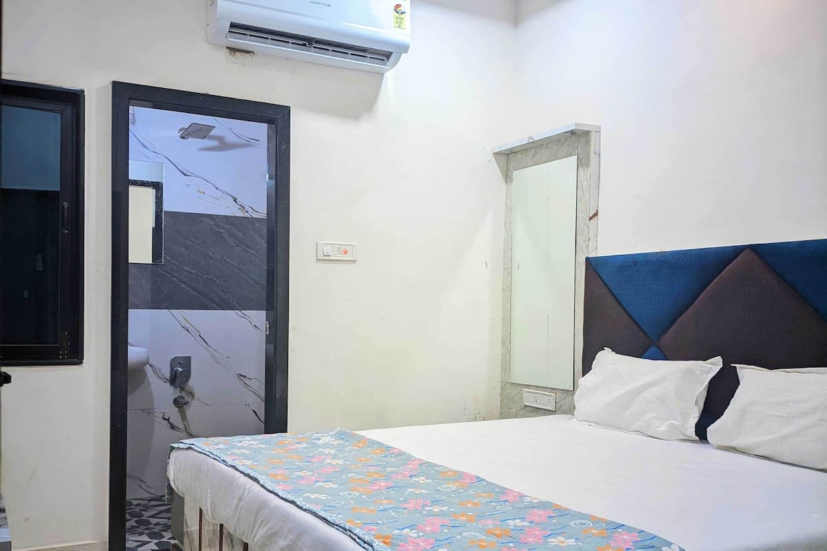 A bedroom with a bed, an air conditioner, a door, and a mirror.
