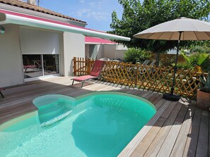 A swimming pool with a wooden deck, a red lounge chair, and a wooden fence. - This charming house, rated 3* by S'I de Royan, features a swimming pool (Vaux-sur-Mer)