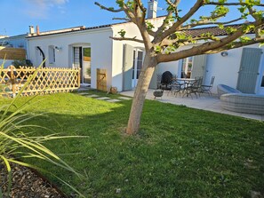 A residential property with a well-maintained lawn, a patio with outdoor furniture, and a white building with a tiled roof.