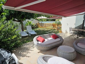 An outdoor patio with wicker furniture, a covered seating area, and a pool in the background. - This charming house, rated 3* by S'I de Royan, features a swimming pool (Vaux-sur-Mer)