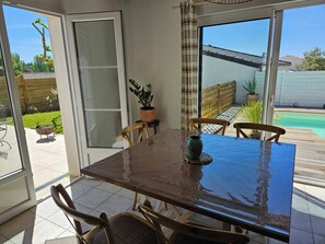 A patio with a table and chairs, a potted plant, and a view of a swimming pool.