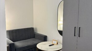 Une petite pièce moderne, avec un canapé gris, une table ronde blanche et un grand miroir au mur.