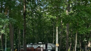 Een grindparkeerplaats die leidt naar een camping met een overdekte camper en een houten terras.
