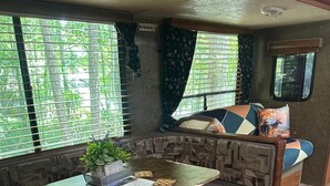 A cozy RV interior with a dining area, seating, and a view of greenery outside. - Slumber Road RV Camper (Jamestown)