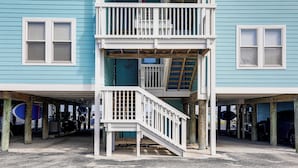 Un immeuble à plusieurs étages, doté d’un escalier et d’un balcon blancs, et comprenant un garage et des planches de surf.