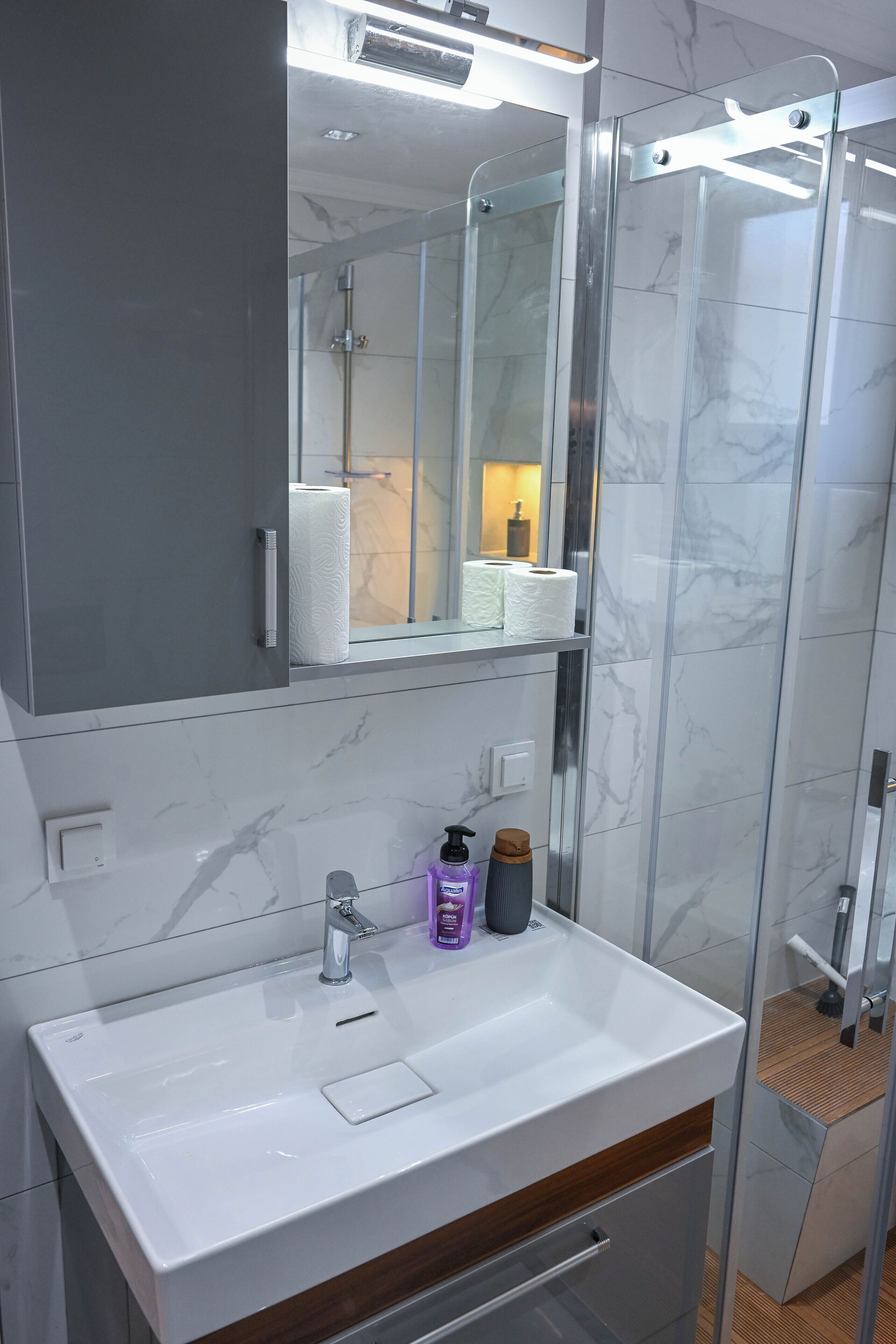 Un baño moderno con un lavabo blanco, un espejo encima y una cabina de ducha de vidrio.
