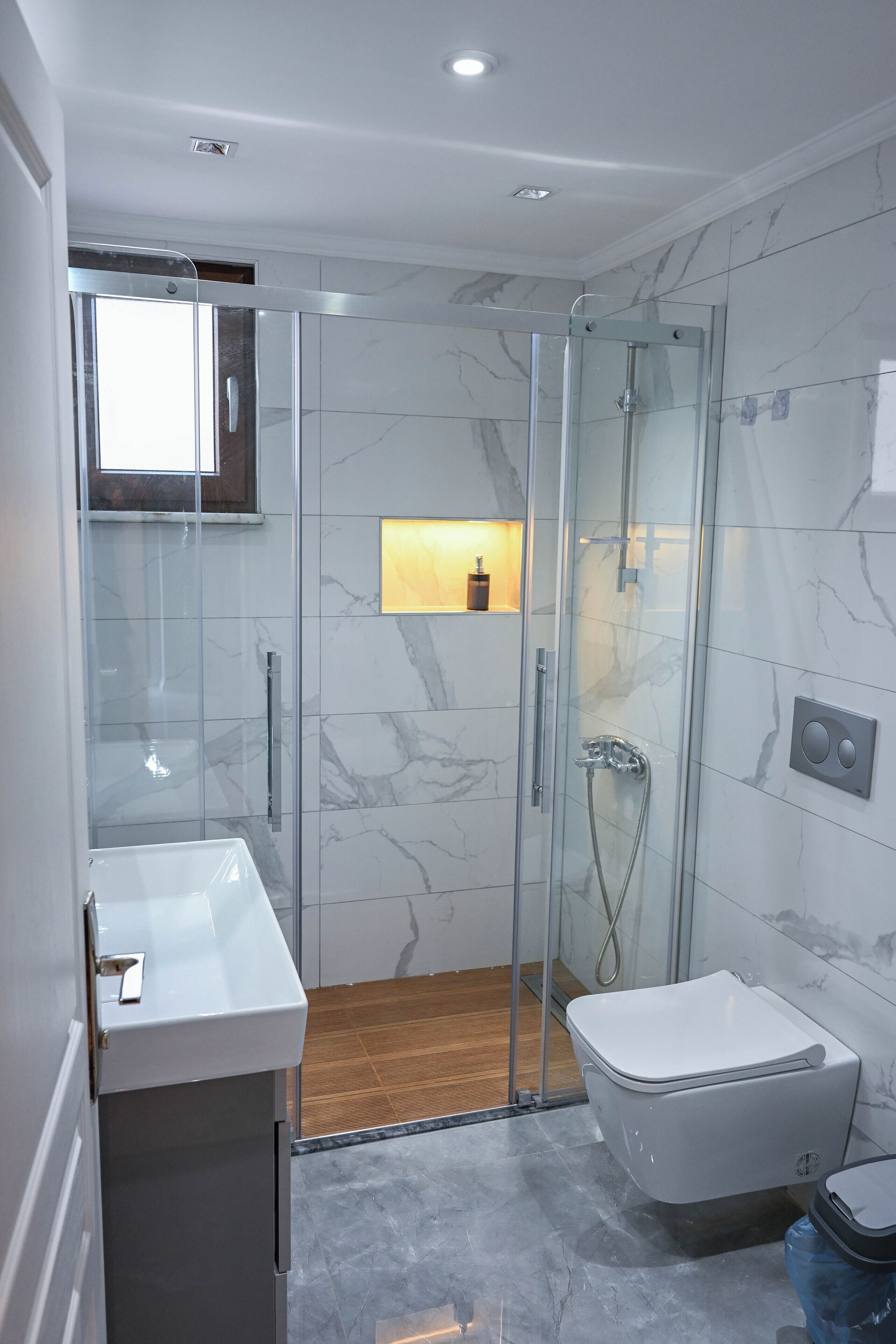 Un baño moderno con ducha de vidrio, lavamanos blanco y retrete.