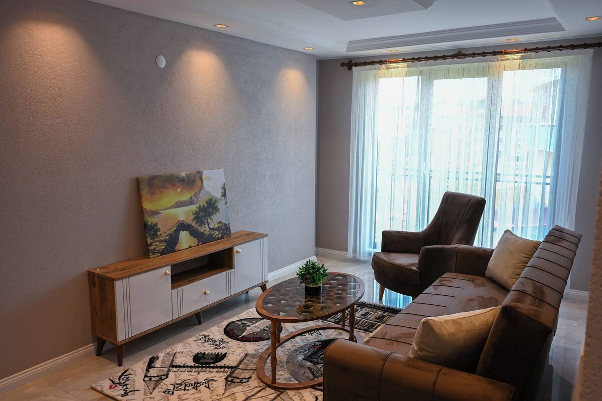 Un salon comprenant un canapé, un fauteuil, une table basse, un meuble pour la télévision et des œuvres d’art.