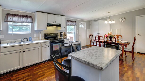A kitchen with white cabinets, a marble island, a dining area with a wooden table and chairs, and a clock on the wall.