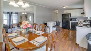 A dining area with a wooden table set for four, surrounded by chairs, and a kitchen area with white cabinets and appliances.