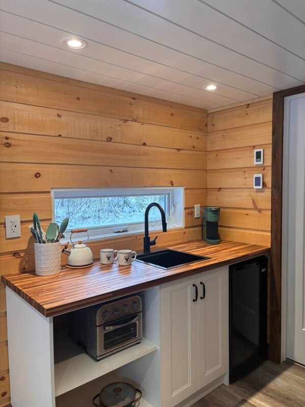 Una cocina compacta con paneles de madera, un lavamanos negro, un ventanal con vistas y una cafetera.