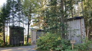 A rustic cabin with a gravel path leading to it, surrounded by dense forest. - Cozy Cabin on Oxtongue River; Wolf Cottage (Huntsville)