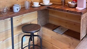 A compact kitchen with wooden walls, a small bar stool, and basic amenities including a coffee maker and a kettle. - Cozy Cabin on Oxtongue River; Wolf Cottage (Huntsville)