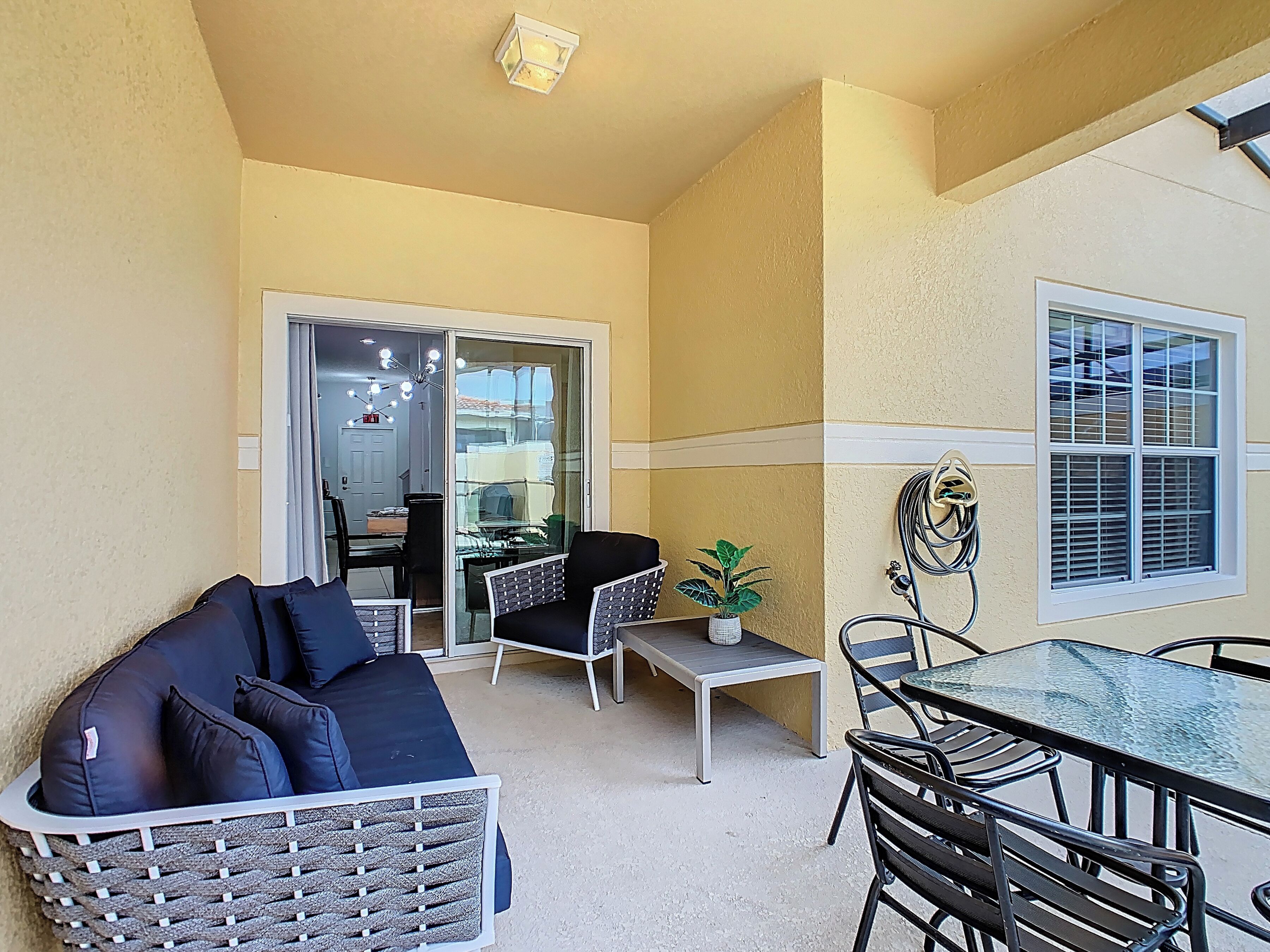 A compact living space with a sofa, dining table, chairs, a small potted plant, and a sliding glass door leading to a kitchen area.