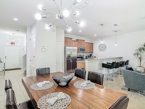 A modern kitchen with a central island, wooden dining table with placemats, and a ceiling light fixture. - Spacious 4-bedroom townhome with fitness room and AC in lovely Kissimmee (Kissimmee)