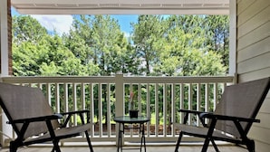 A covered porch with two chairs and a small table, overlooking a wooded area.