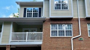 A two-story residential building with a brick facade, a balcony on the upper floor, and two attached garages.