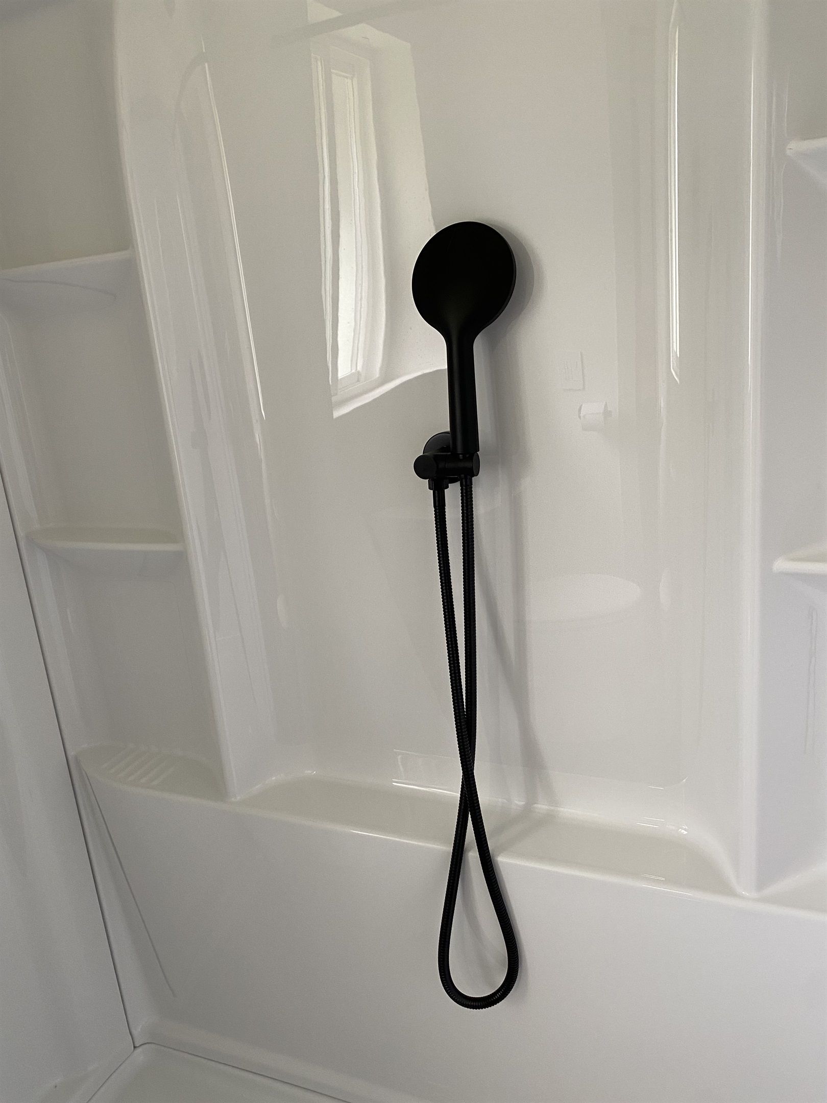 A showerhead mounted on a white wall with a clear glass door.