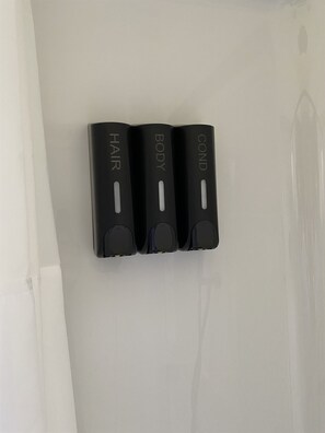 Three black wall-mounted dispensers labeled 'HAIR,' 'BODY,' and 'COND' on a white wall.