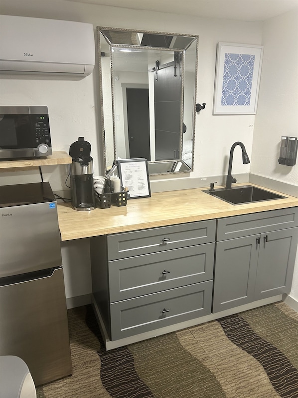 A compact kitchenette with a microwave, coffee maker, and a framed welcome sign.