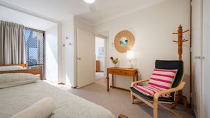 Un dormitorio con cama, una silla, una mesa y una lámpara de pared.