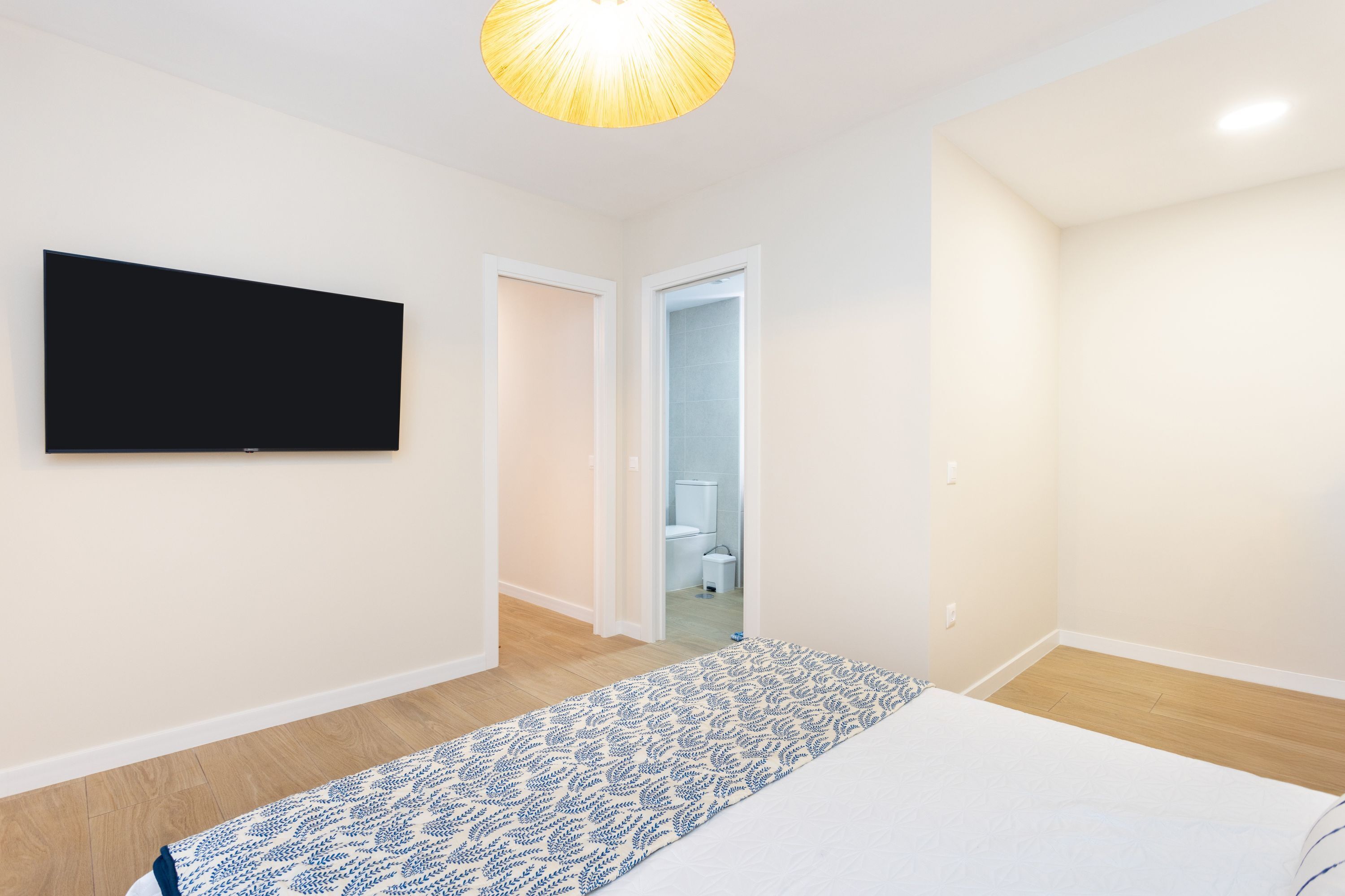 Un dormitorio con una cama, un televisor montado en la pared y un pasillo que conduce a un baño.
