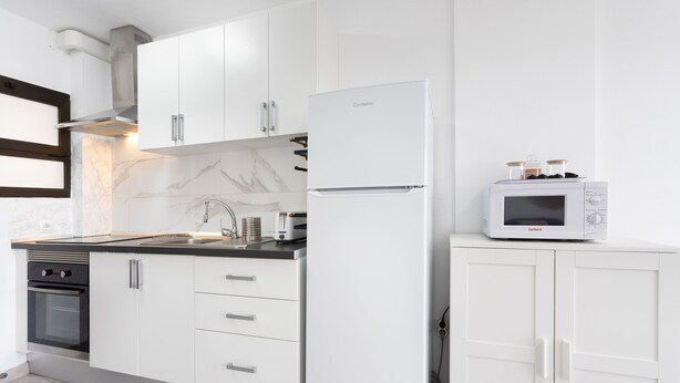 Une cuisine moderne avec des meubles blancs, un four encastré, un four à micro-ondes et un grille-pain.