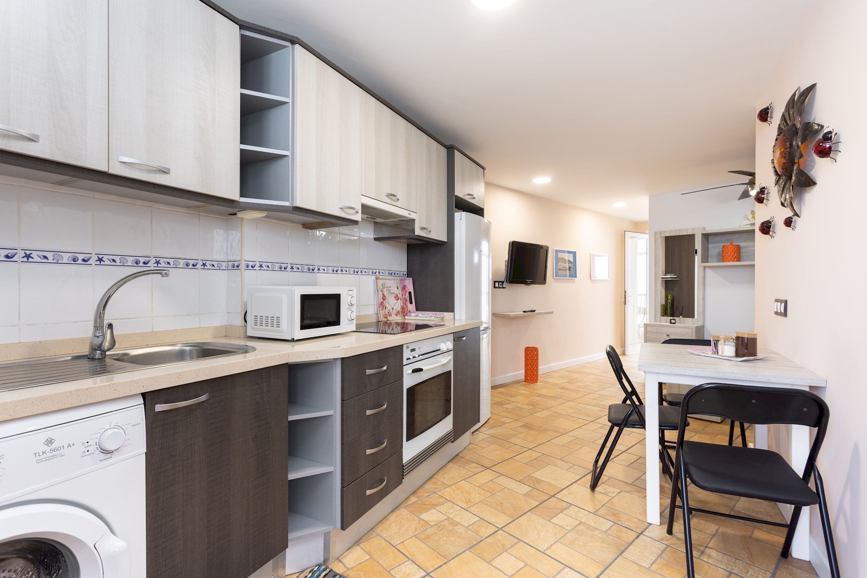 A compact kitchen with a sink, microwave, and a washing machine. There is a dining area with a table and chairs.