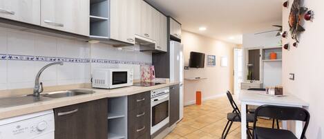 A compact kitchen with a sink, microwave, and a washing machine. There is a dining area with a table and chairs.