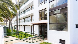 A modern building with multiple floors, large windows, and a green outdoor area with stairs and railings.