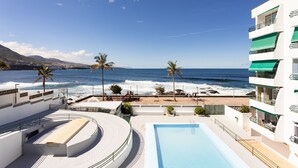A pool area with a view of the ocean, palm trees, and a building with balconies.