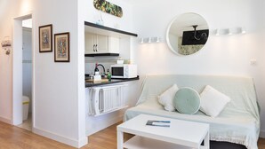 A compact living space with a kitchenette, a round mirror, and a sofa with cushions.