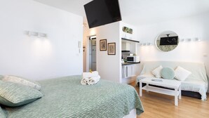 A bedroom with a bed, a TV mounted on the wall, a sofa, and a small table.