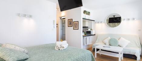 A bedroom with a bed, a TV mounted on the wall, a sofa, and a small table.