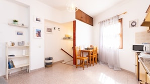 Une cuisine lumineuse et bien éclairée, avec une table à manger, des chaises et un four à micro-ondes. Un escalier mène à un autre niveau, et une étagère contient des livres et des objets décoratifs.