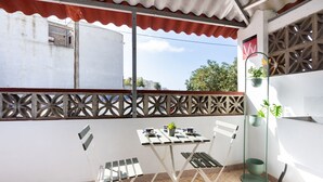Un balcon avec une table et des chaises blanches, une plante en pot et une étagère en métal.
