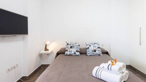 A hotel room with a bed, a nightstand, a wall-mounted TV, and a small shelf with a lamp. - Apartamento Brisa del Mar (Tacoronte)