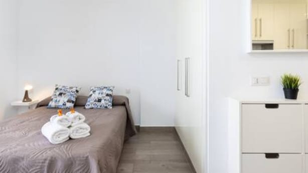 A modern hotel room with a neatly made bed, a bedside table with a lamp, a small cabinet, and a potted plant. - Apartamento Brisa del Mar (Tacoronte)