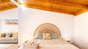 Een slaapkamer met een groot bed, een houten plafond, een bank en een kleine tafel met een lamp.
